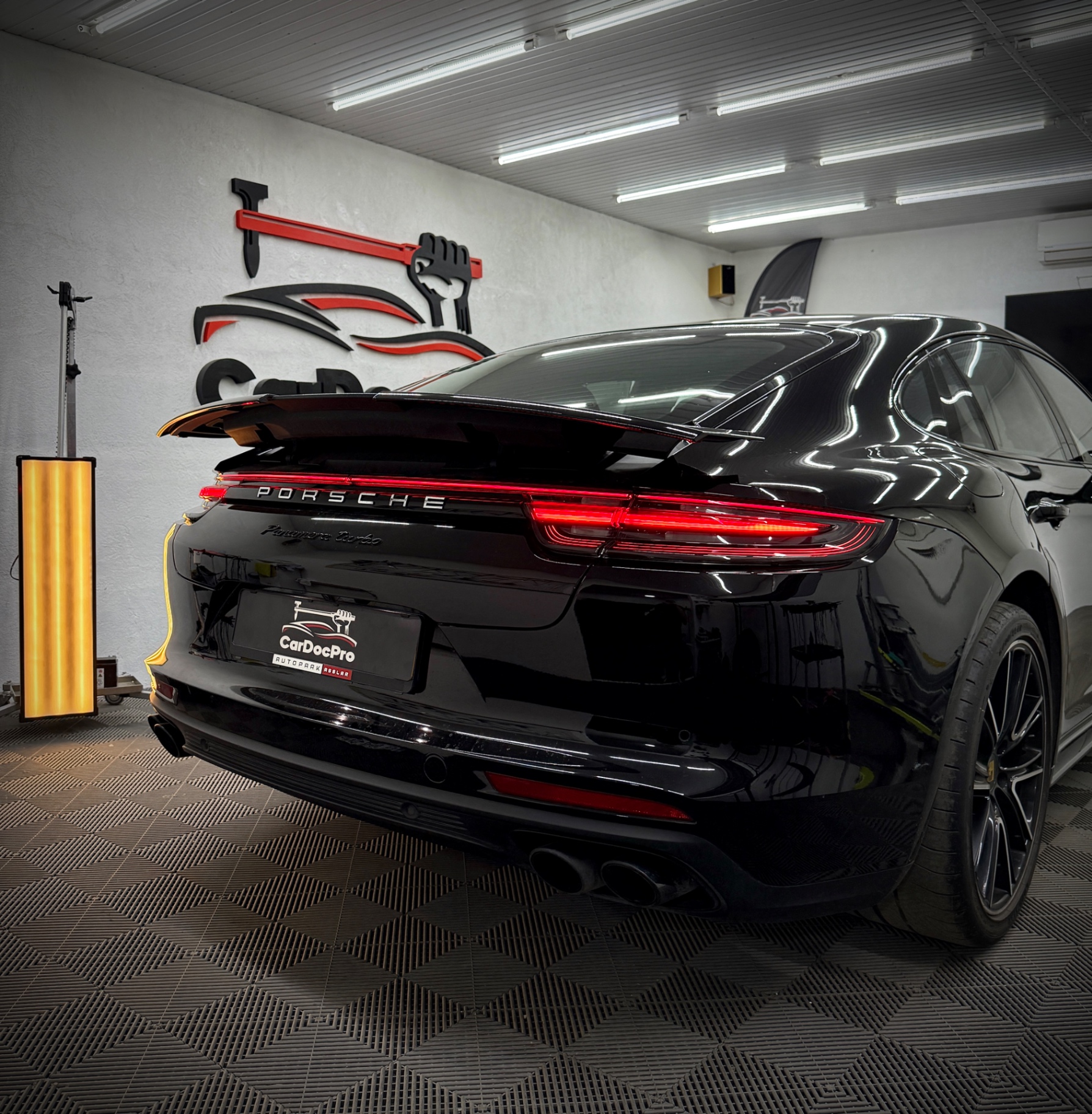 Porsche Panamera Turbo negru în atelierul CarDocPro, cu logo-ul pe perete și lampa PDR